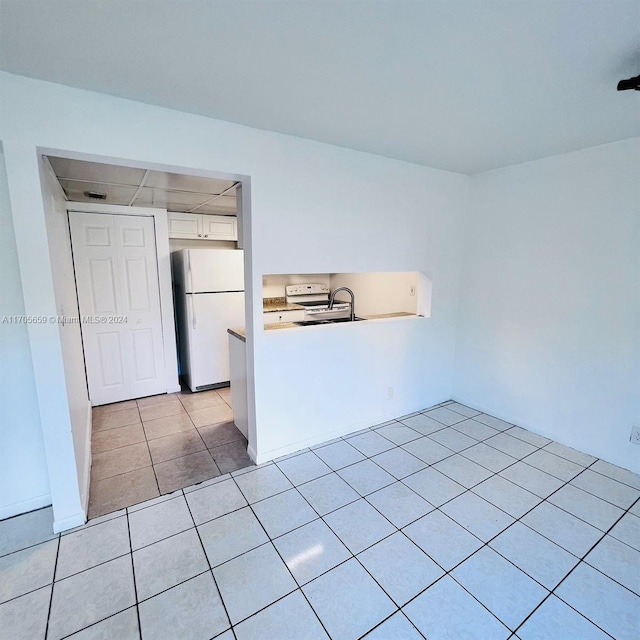 kitchen with kitchen peninsula, sink, light tile patterned floors, white refrigerator, and white cabinets