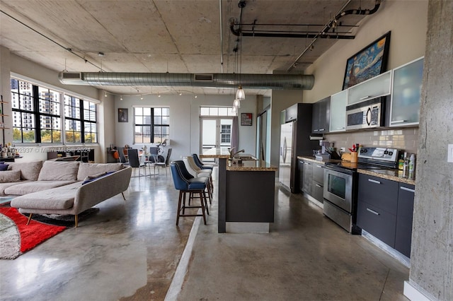 kitchen featuring sink, light stone counters, appliances with stainless steel finishes, decorative light fixtures, and a kitchen bar