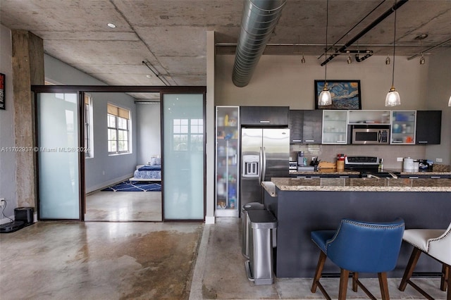 kitchen featuring light stone countertops, hanging light fixtures, stainless steel appliances, kitchen peninsula, and a kitchen bar