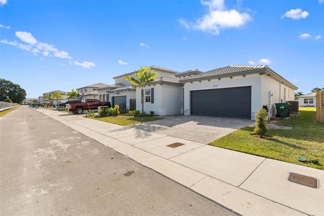 view of front facade featuring stucco siding, a front lawn, a tile roof, decorative driveway, and a garage