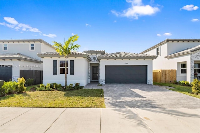 mediterranean / spanish-style home featuring stucco siding, a tile roof, decorative driveway, fence, and an attached garage