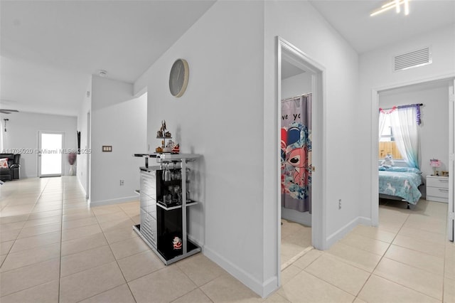 hall with light tile patterned floors, visible vents, and baseboards