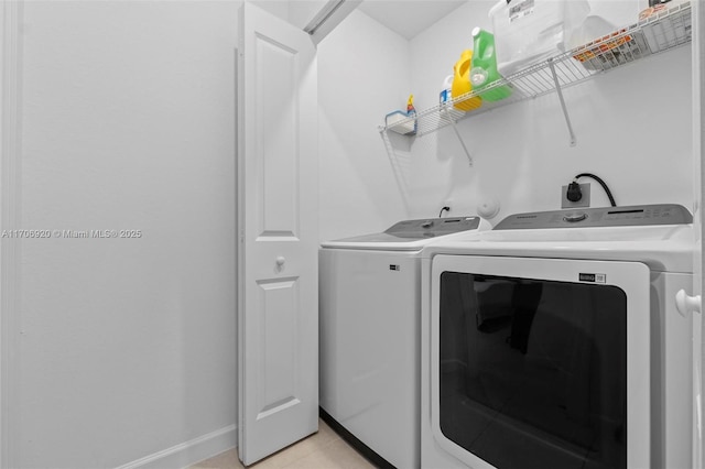 washroom featuring light tile patterned floors, laundry area, washing machine and dryer, and baseboards