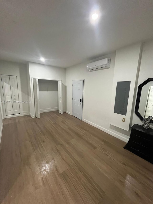 unfurnished living room with a wall unit AC, electric panel, wood finished floors, and baseboards