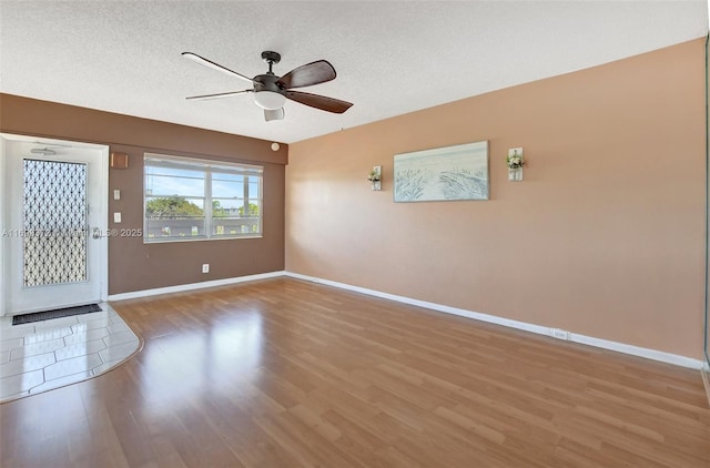 interior space featuring ceiling fan, a textured ceiling, baseboards, and wood finished floors