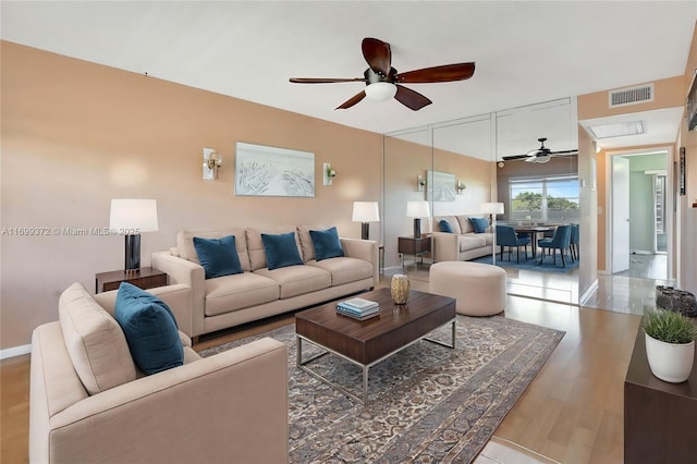 living area with a ceiling fan, wood finished floors, visible vents, and baseboards