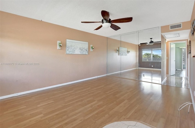 unfurnished room featuring a ceiling fan, wood finished floors, visible vents, baseboards, and a textured ceiling