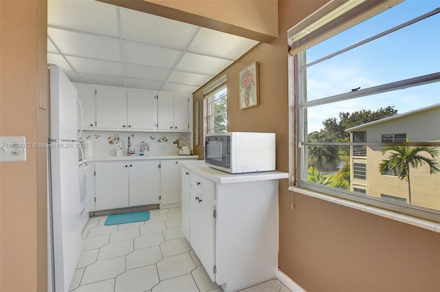 kitchen with sink, white refrigerator, white cabinets, backsplash, and a drop ceiling