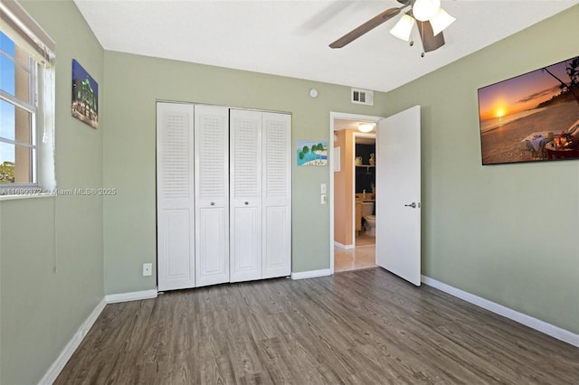 unfurnished bedroom with wood finished floors, visible vents, a closet, and baseboards