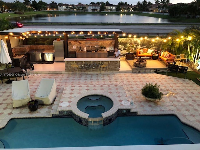 view of swimming pool featuring an in ground hot tub, a patio area, an outdoor fire pit, and a water view