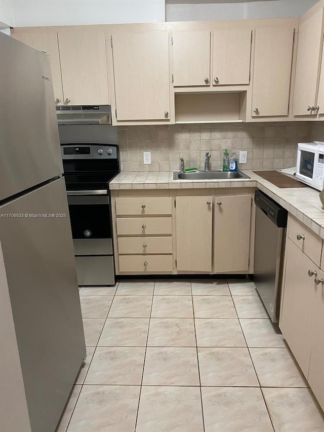 kitchen with tasteful backsplash, sink, stainless steel appliances, tile counters, and light tile patterned floors