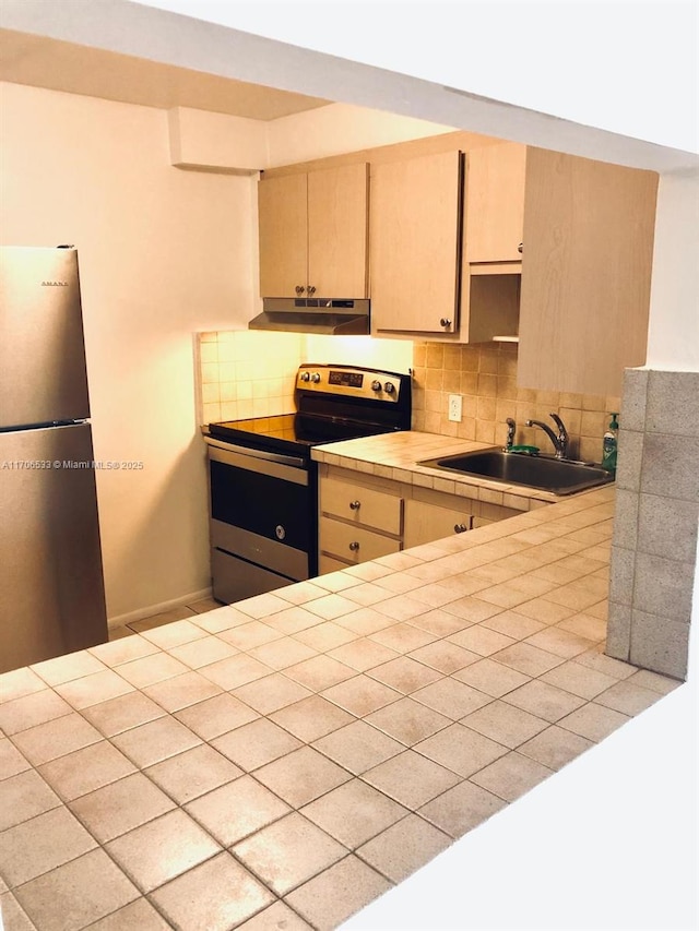 kitchen with tile countertops, appliances with stainless steel finishes, tasteful backsplash, light brown cabinetry, and sink