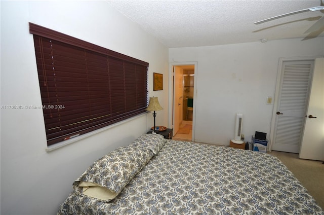 carpeted bedroom with ceiling fan, ensuite bathroom, and a textured ceiling