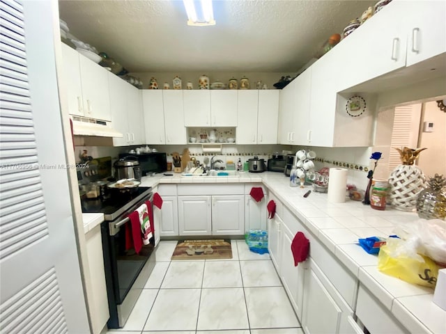 kitchen featuring stainless steel range with electric stovetop, tile countertops, light tile patterned floors, a textured ceiling, and white cabinetry