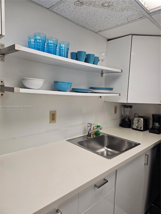 kitchen with a paneled ceiling, white cabinetry, and sink