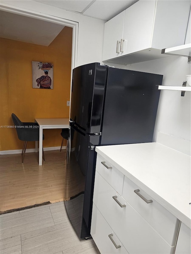 kitchen with white cabinetry, black refrigerator, and light hardwood / wood-style floors