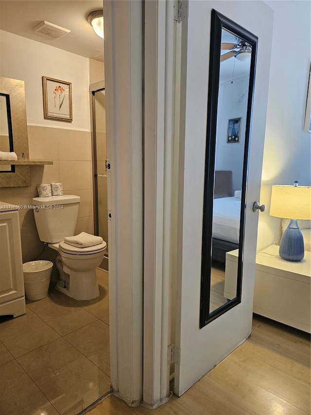 bathroom with an enclosed shower, ceiling fan, wood-type flooring, tile walls, and toilet