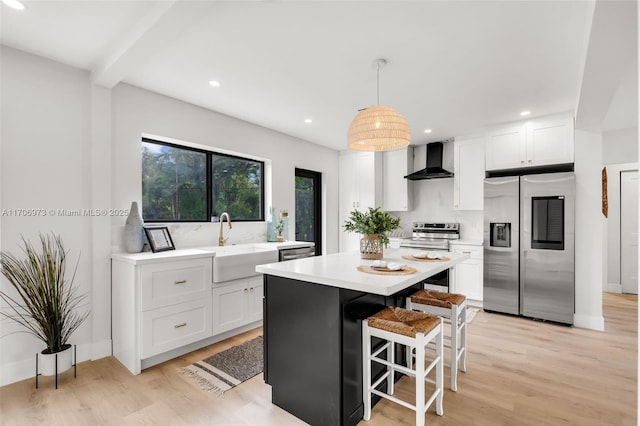 kitchen featuring wall chimney exhaust hood, stainless steel appliances, hanging light fixtures, and white cabinets