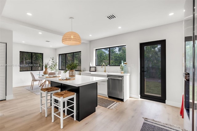 kitchen featuring a breakfast bar, white cabinetry, dishwasher, a kitchen island, and pendant lighting