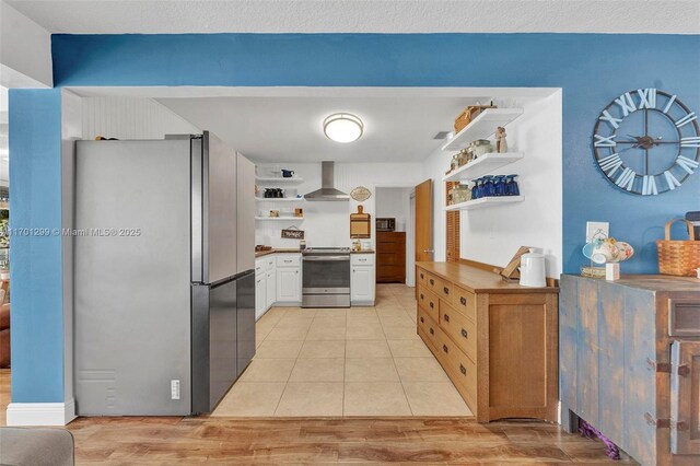 kitchen with white cabinets, wall chimney exhaust hood, light hardwood / wood-style floors, and appliances with stainless steel finishes