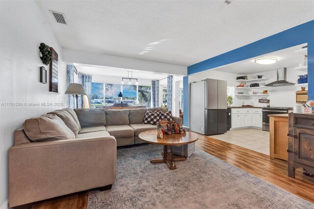 living room with light hardwood / wood-style floors, a textured ceiling, and an inviting chandelier