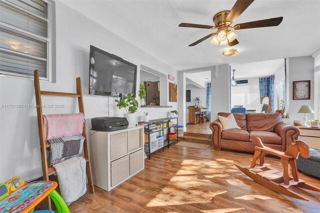 living room with ceiling fan, light hardwood / wood-style floors, and a textured ceiling