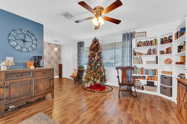 living area featuring wood-type flooring, a textured ceiling, and ceiling fan