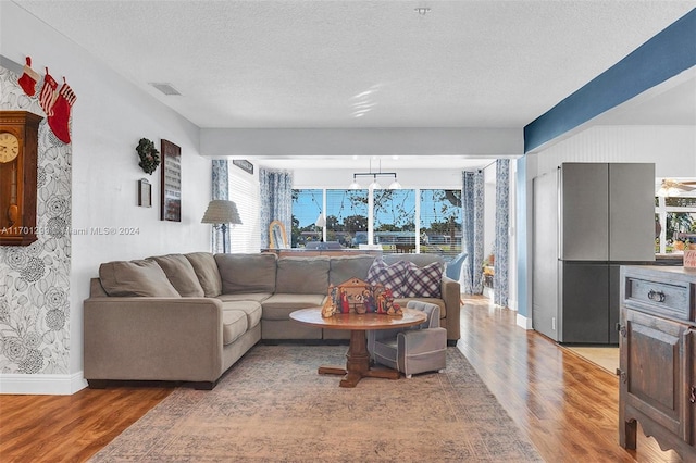 living room featuring a notable chandelier, light wood-type flooring, and a textured ceiling