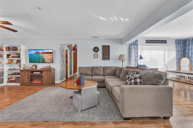 living room featuring ceiling fan, light wood-type flooring, and a textured ceiling