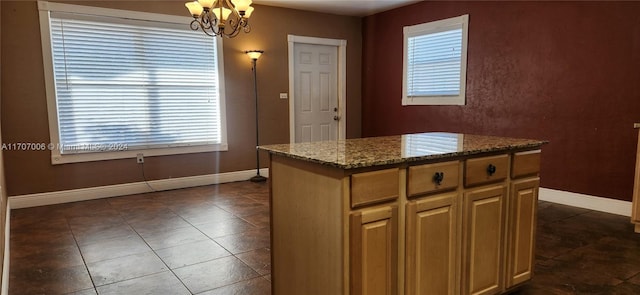 kitchen featuring light stone countertops, a center island, dark tile patterned flooring, and an inviting chandelier