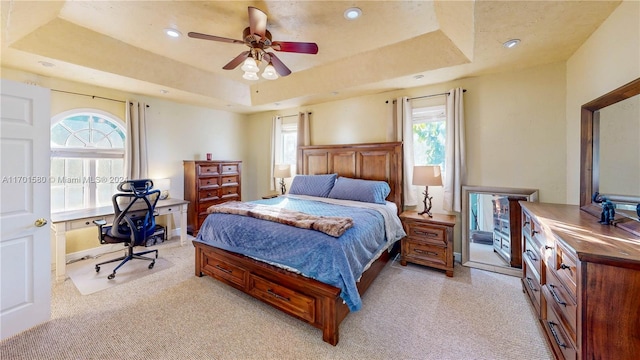 bedroom with a raised ceiling, ceiling fan, and light carpet