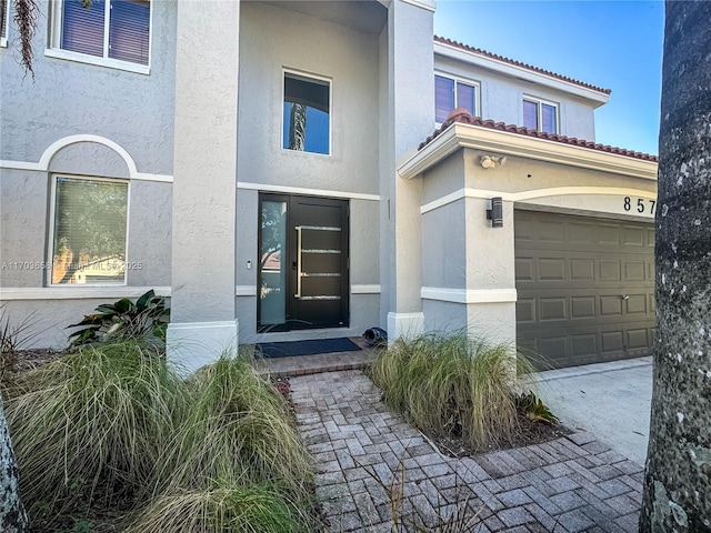 view of exterior entry with stucco siding, an attached garage, and a tile roof