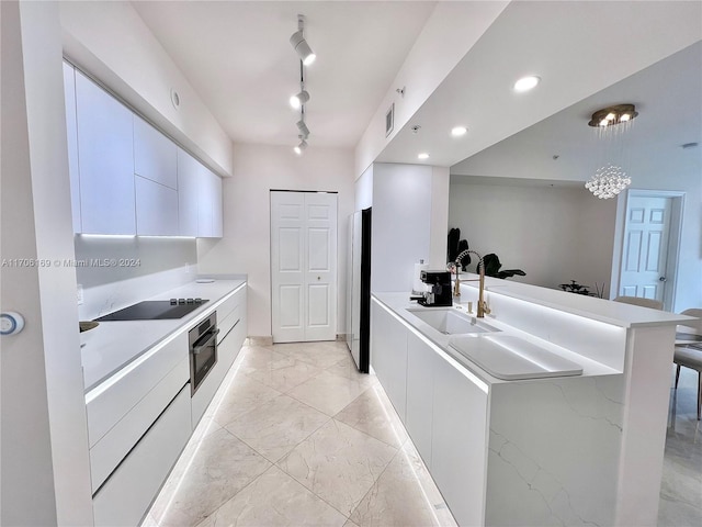 kitchen featuring track lighting, sink, black appliances, white cabinets, and hanging light fixtures