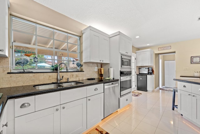 kitchen with decorative backsplash, stainless steel appliances, sink, light tile patterned floors, and white cabinetry