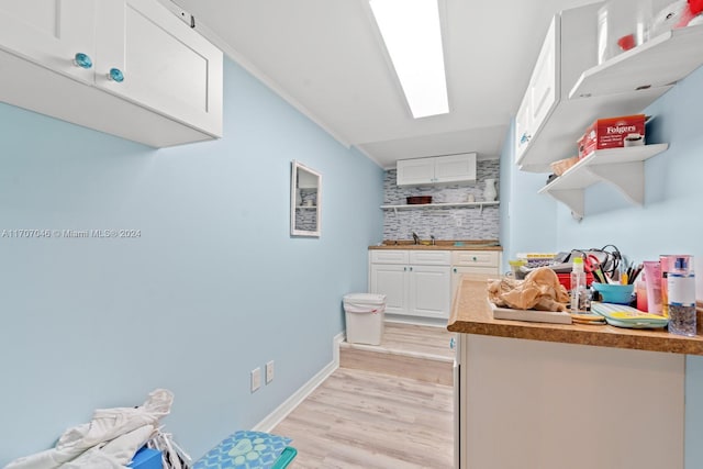 kitchen with white cabinets, sink, crown molding, and light hardwood / wood-style flooring