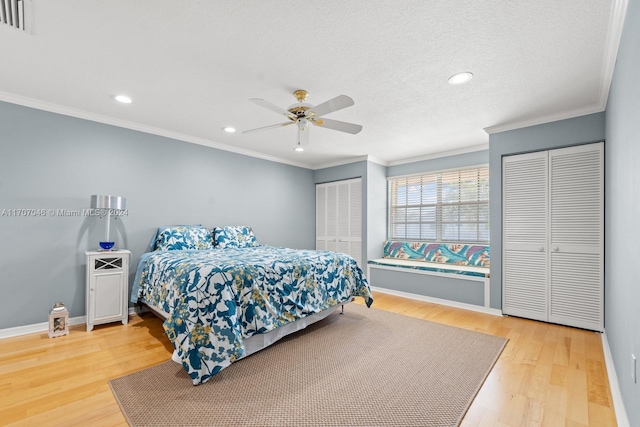 bedroom with hardwood / wood-style floors, two closets, ceiling fan, and crown molding