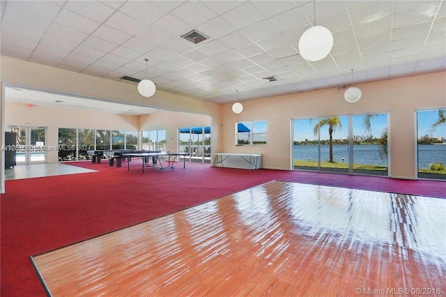 workout area with wood-type flooring, a water view, and a drop ceiling