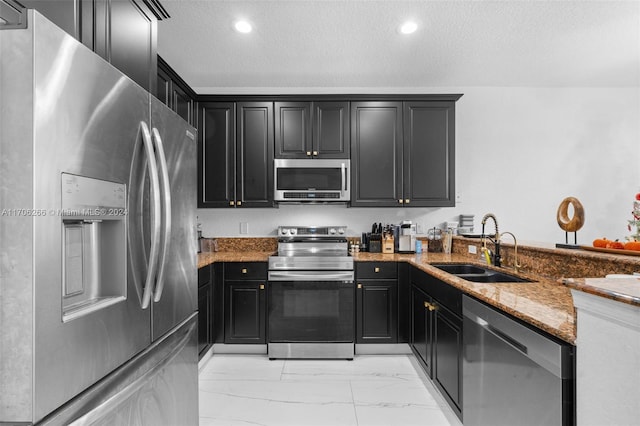 kitchen with light stone countertops, appliances with stainless steel finishes, a textured ceiling, and sink