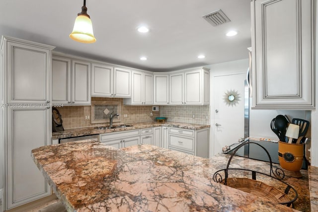 kitchen with pendant lighting, light stone counters, sink, and tasteful backsplash