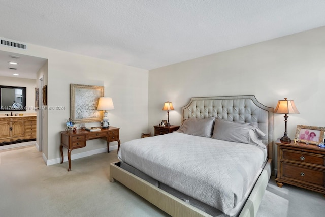 bedroom with a textured ceiling, sink, light carpet, and ensuite bath