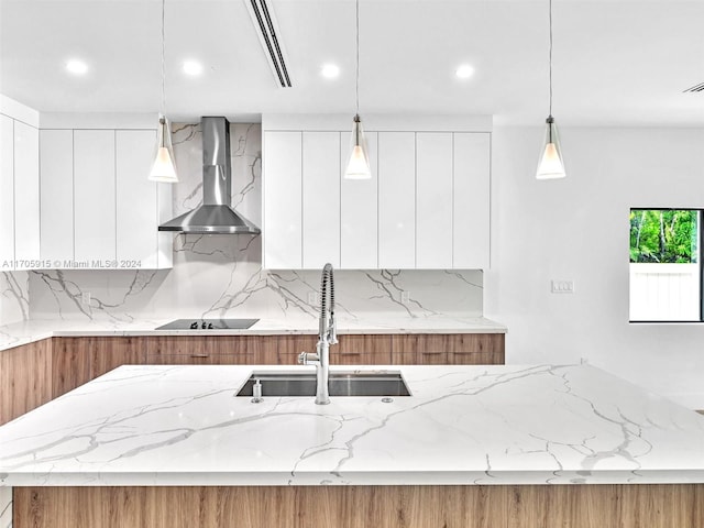 kitchen with sink, wall chimney exhaust hood, stovetop, decorative light fixtures, and white cabinets