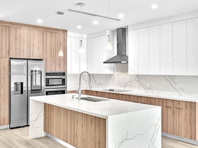 kitchen with sink, wall chimney exhaust hood, stainless steel appliances, an island with sink, and pendant lighting