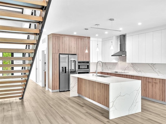 kitchen featuring a center island with sink, wall chimney range hood, sink, hanging light fixtures, and high quality fridge