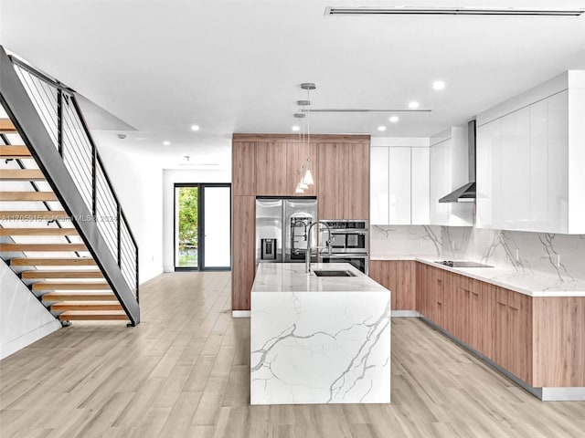 kitchen with light stone countertops, pendant lighting, a center island with sink, light hardwood / wood-style floors, and white cabinetry