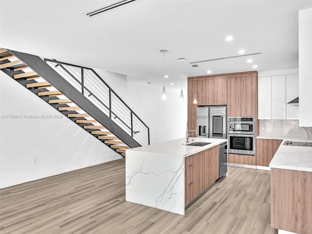 kitchen featuring a spacious island, hanging light fixtures, light hardwood / wood-style flooring, light stone countertops, and white cabinetry