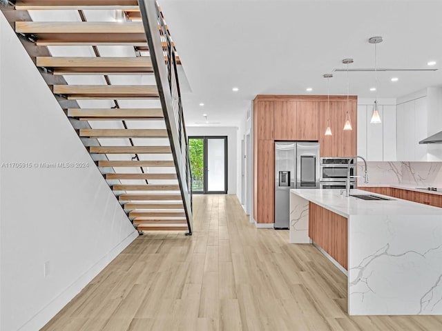 kitchen featuring light stone countertops, high end refrigerator, decorative light fixtures, light hardwood / wood-style floors, and white cabinetry