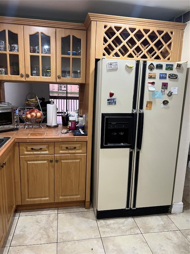 kitchen with tile countertops, light tile patterned flooring, and white fridge with ice dispenser