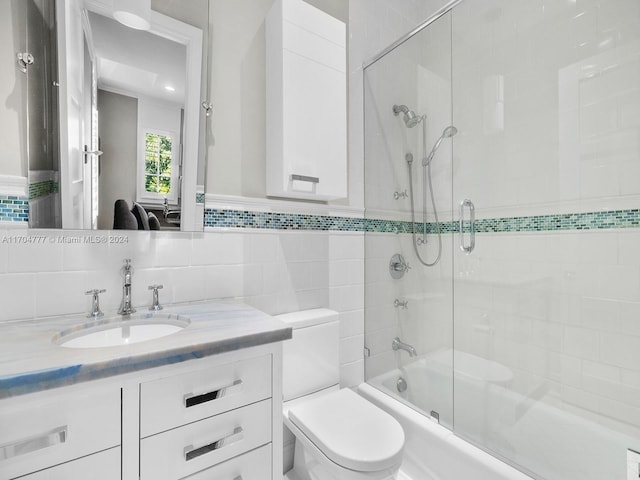 full bathroom with shower / bath combination with glass door, vanity, toilet, and tile walls