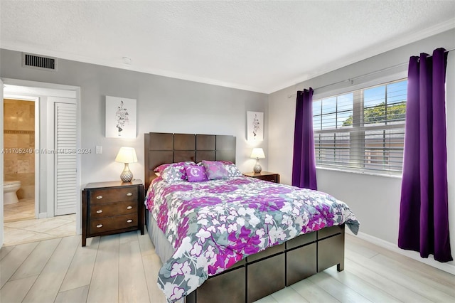 bedroom featuring a textured ceiling, connected bathroom, light hardwood / wood-style flooring, and ornamental molding