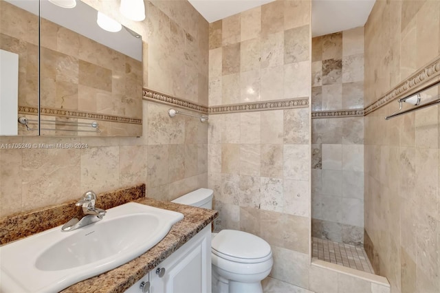 bathroom featuring toilet, a tile shower, tile walls, and vanity